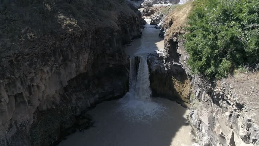 Waterfall flows into the river below under the bright sun