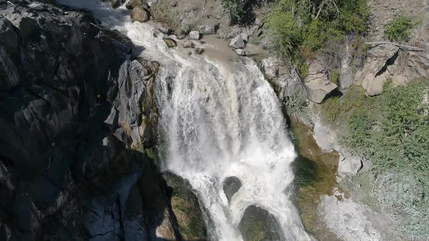 Waterfall flows over cliff through rough stone terrain