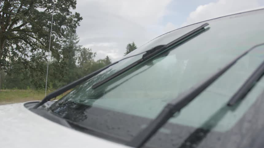 Windshield wipers sweep back and forth across the front windshield of a vehicle