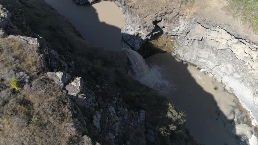 Water flows into a muddy ravine on a sunny day
