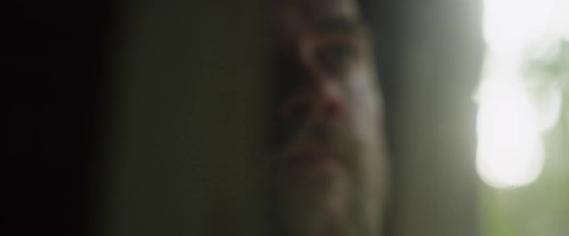 A man runs his hand through his hair while sitting next to a window