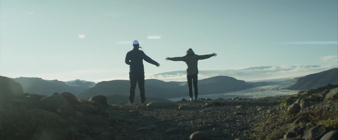 A pair of hikers playing around near a cliff in the mountains