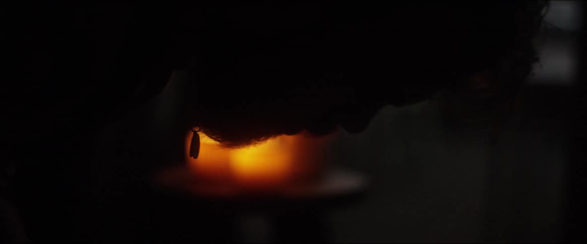 A man is bent over with candles flickering behind him