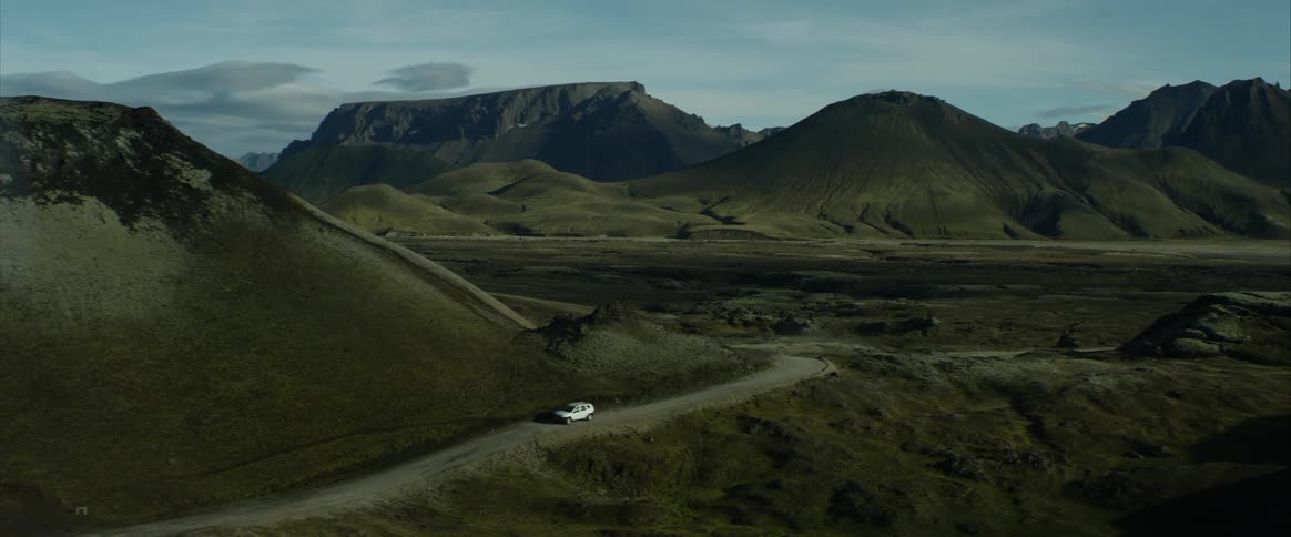 Car drives along dirt road winding through green hills