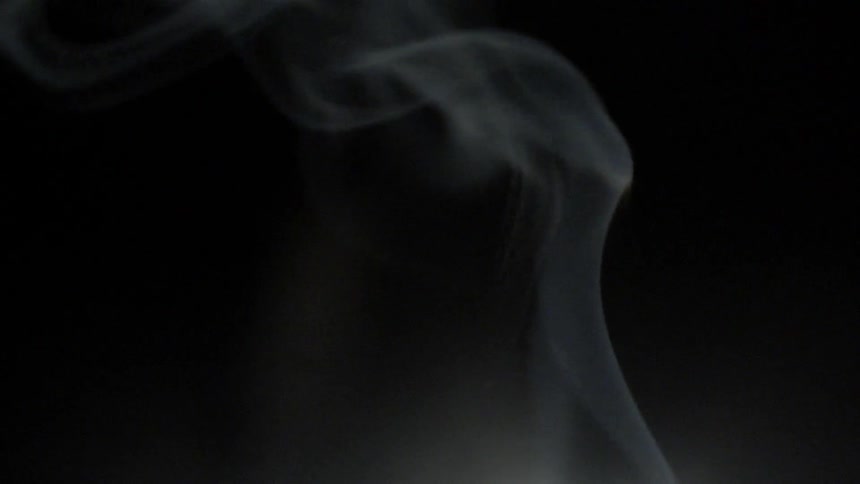 A stream of white smoke rises in front of a black background