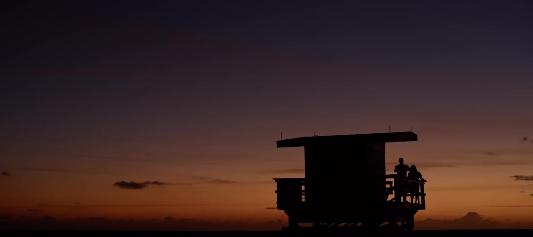 People stand on balcony of small building against the orange sky