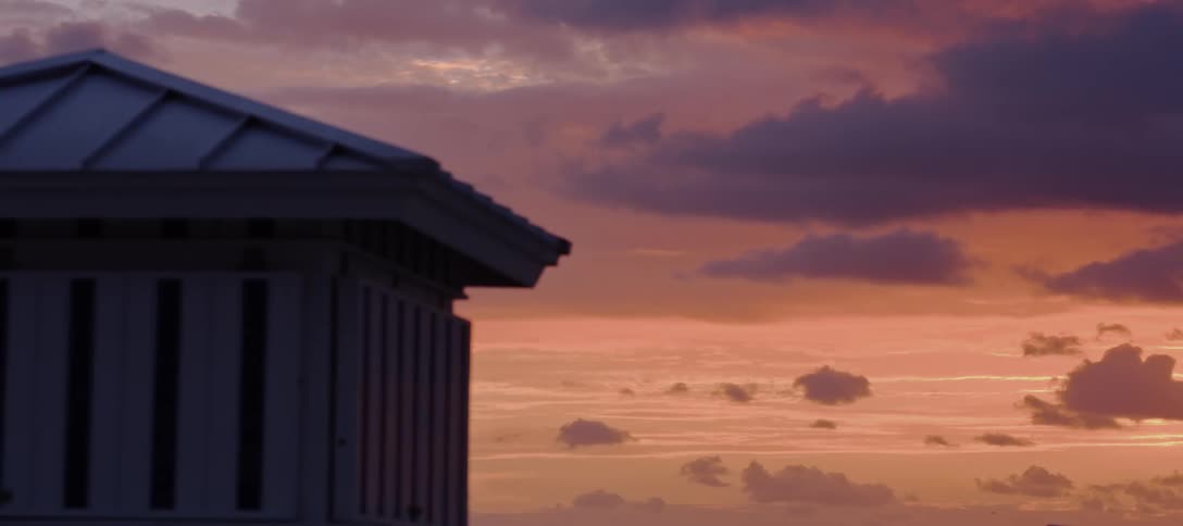 Clouds float in the sky behind a building as the sun lies below the horizon