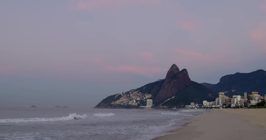 Ipanema beach shoreline at sunrise with waves crashing ashore and mountain backdrop