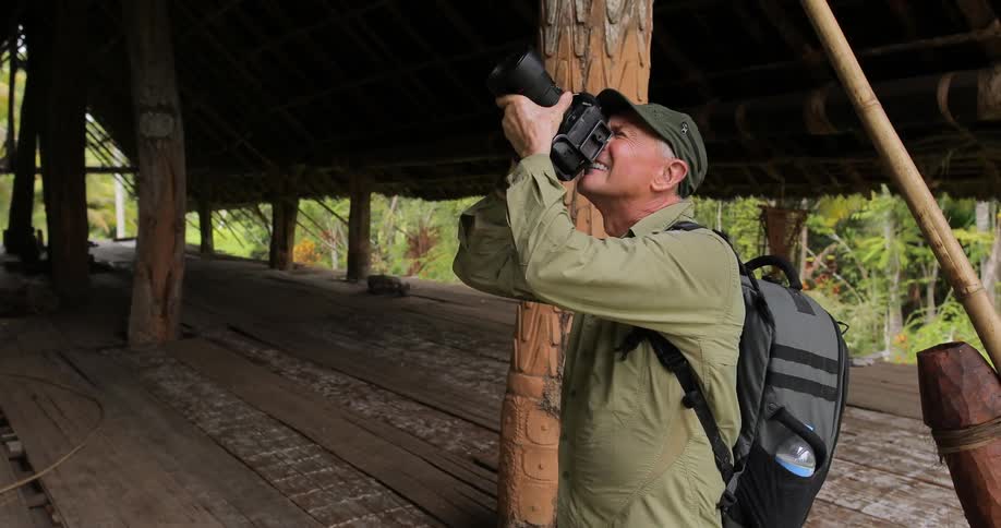 A man in a backpack taking pictures of a hut