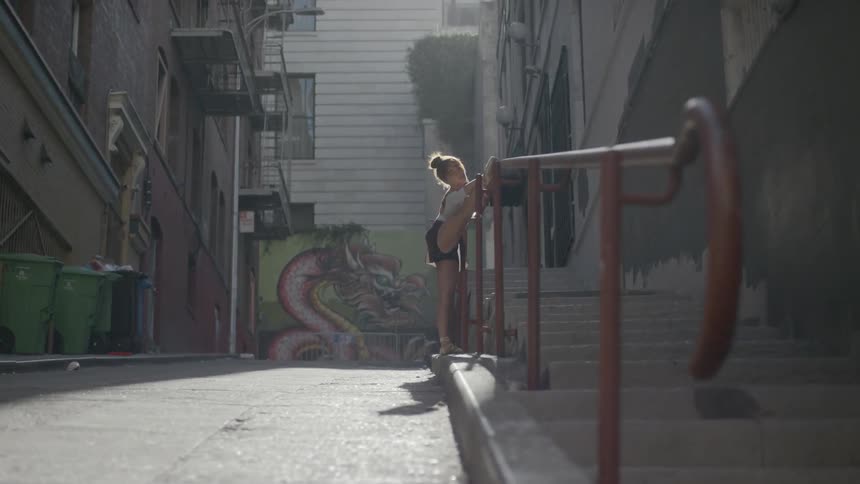 Dancer stretches in alley using hand rail as dance bar