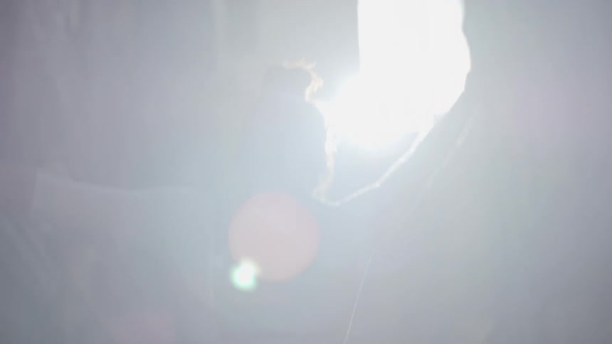 A ballet dancer dances in an alley between apartment buildings as the sun shines down