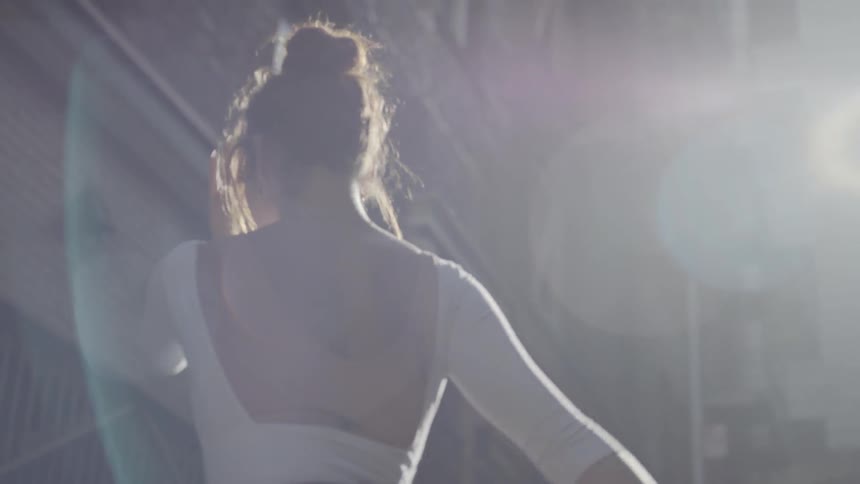 Dancer stretches under glare from the sun next to a building