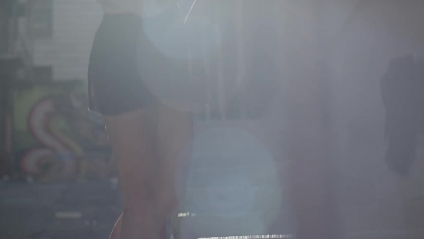 A ballet dance gets on her toes while holding a handrail next to a staircase in a dingy alley