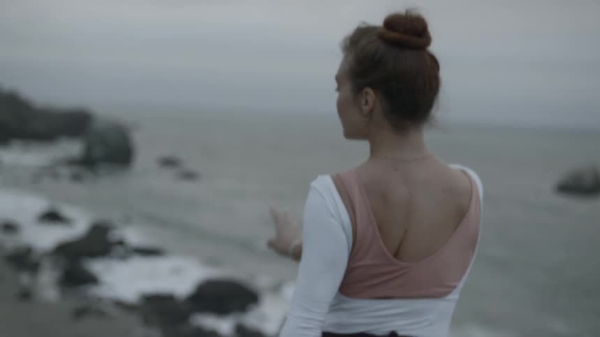 A woman dances on the beach on a windy cloudy day