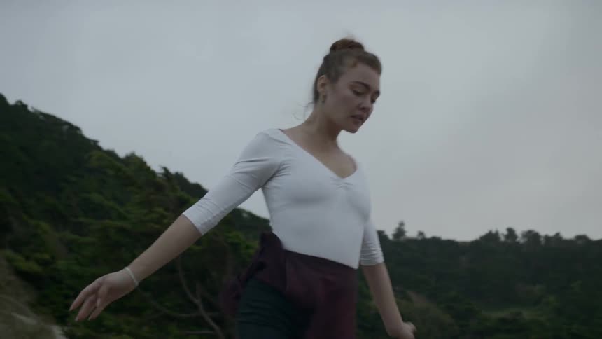 Ballerina wearing a white leotard gracefully dances outside near forest trees on a cloudy day
