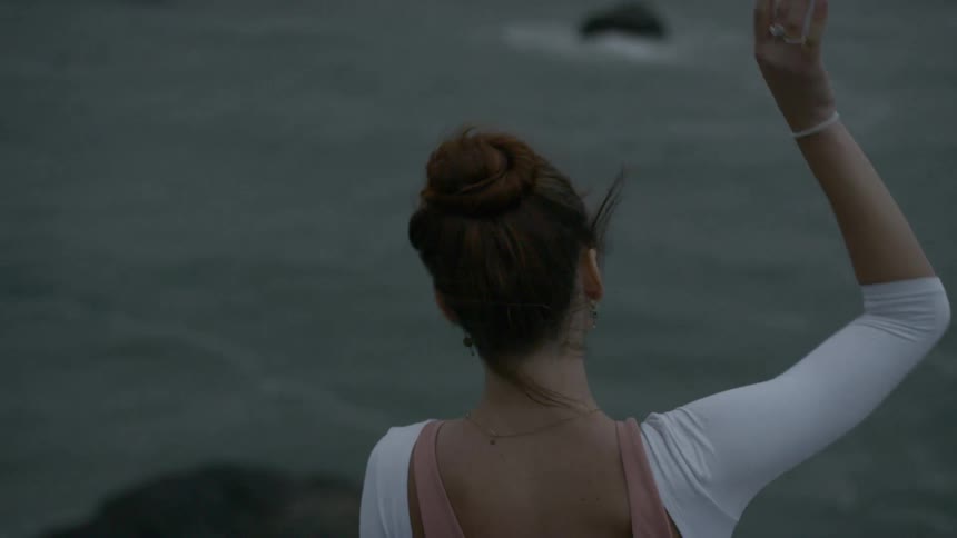 Ballerina warms up before dancing on a hill next to the seashore on a cloudy day