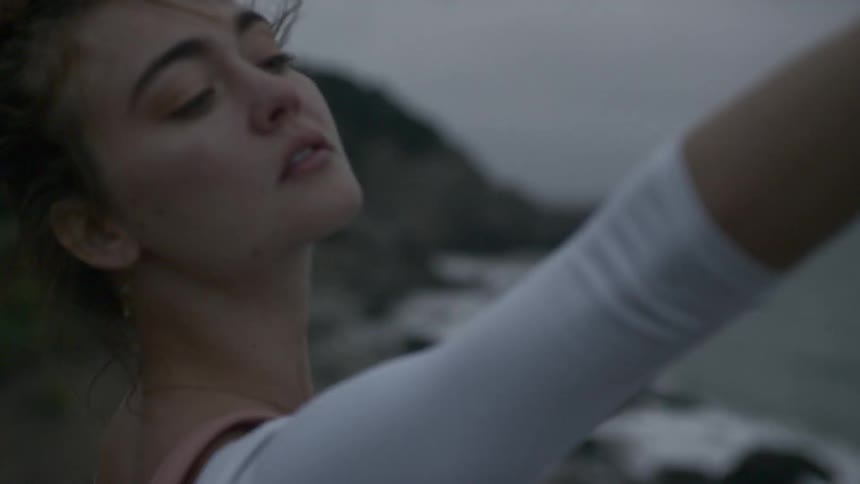Woman dances on shore under cloudy sky