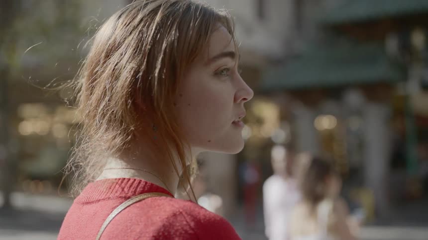 A woman stands in a city street and looks around as pedestrians walk