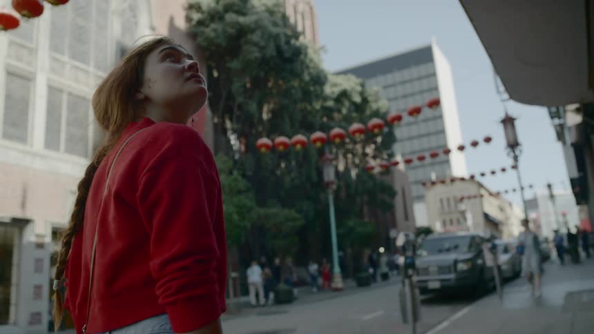 Blonde woman wearing a red sweater walks down the street and looks around curiously in the city