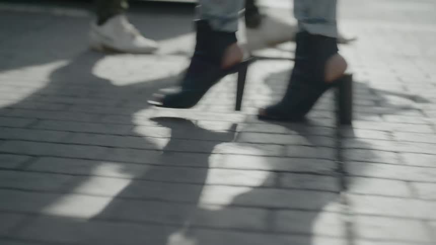 Brown designer high heels stand out among other footwear as pedestrians walk across an outdoor plaza on a sunny day