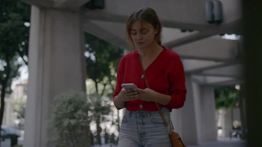 A young woman walks past a building with large concrete pillars