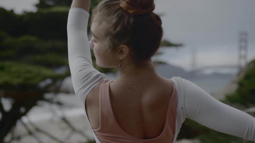 A woman with auburn hair performs a ballet routine outside