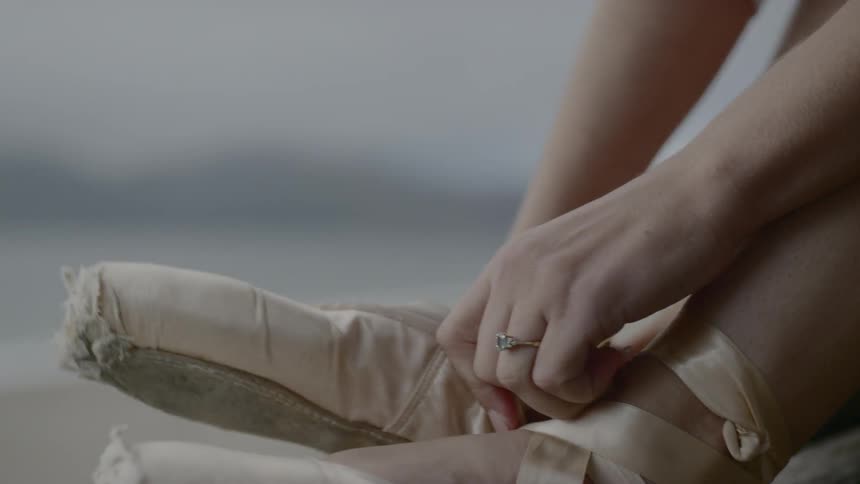 A young woman putting on pointe shoes while sitting down outdoors