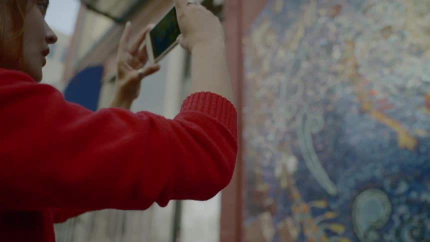 A woman takes a picture of a mural with her cell phone