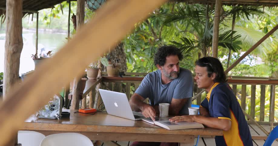 Two men work and talk at a table outside