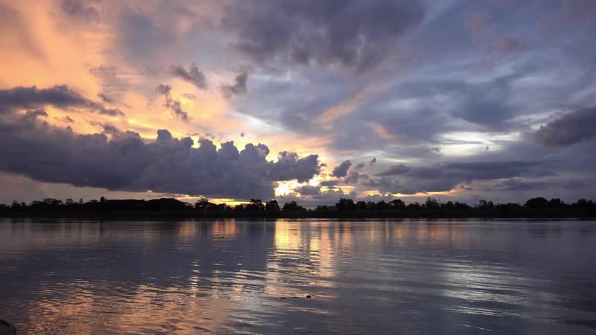 Sun going down on a cloudy day overlooking a calm water body