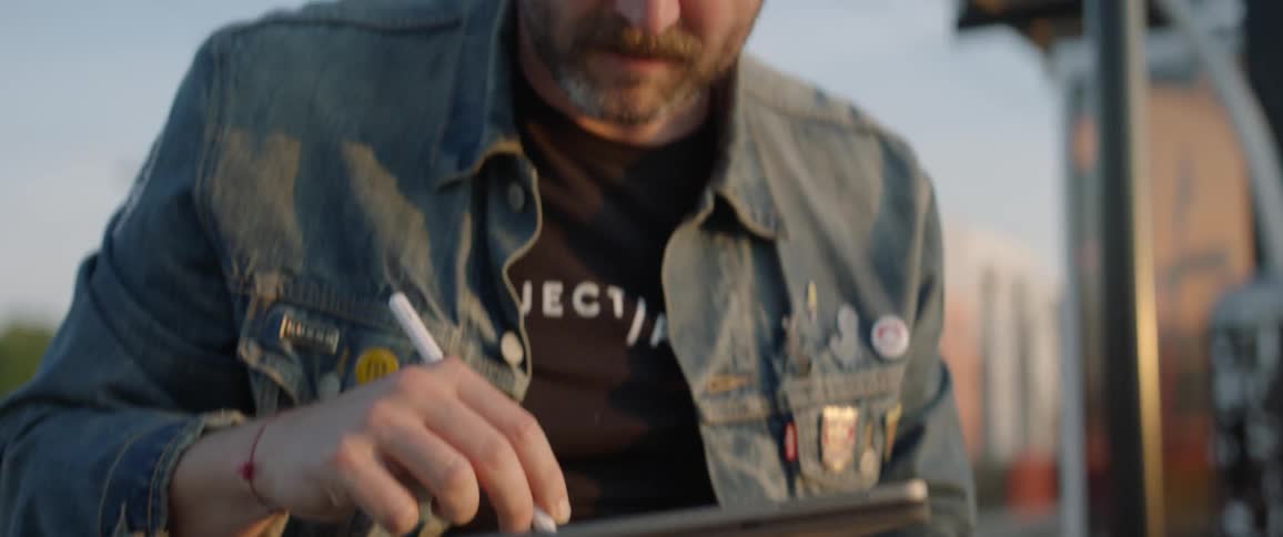 A man sitting down outside drawing on a tablet