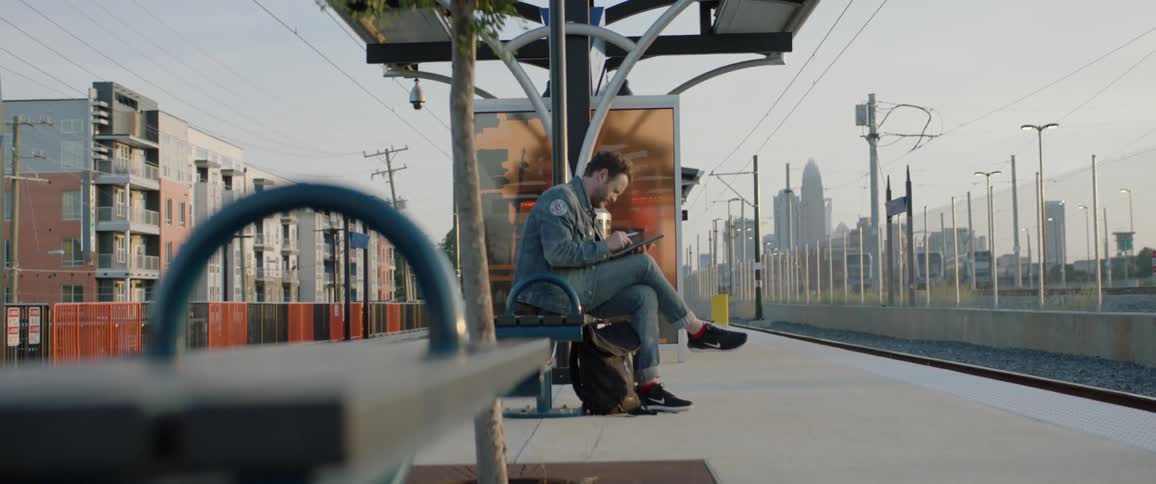 A man sitting while waiting for a train on this phone