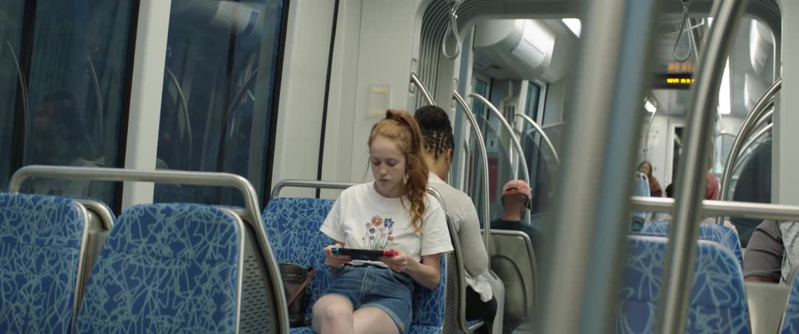 A teenage girl plays a portable video game while sitting on a train