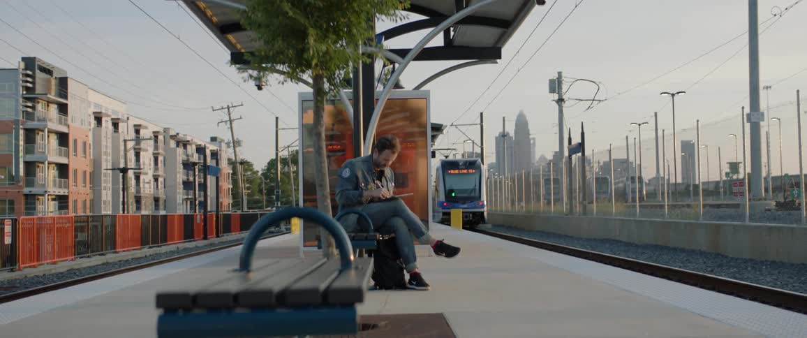 A man sits on a bench at a train station taking notes on paper