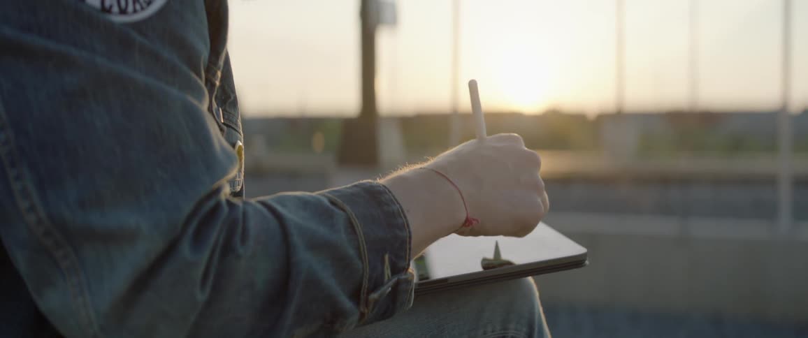A young man sits outside and draws on a tablet