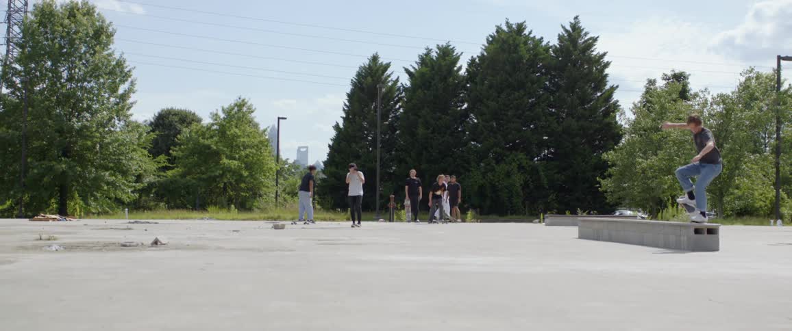 Man films skateboarders performing tricks on outdoor lot