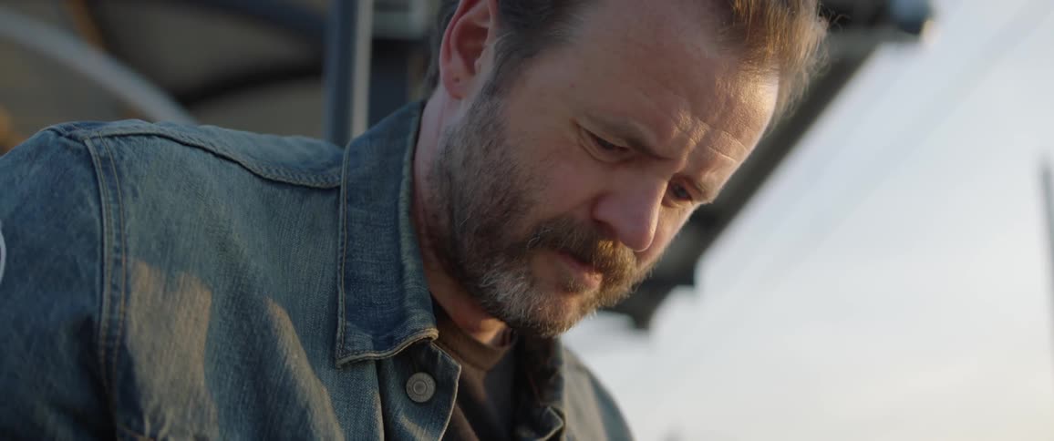 Man wearing jean jacket with patch writes outdoors