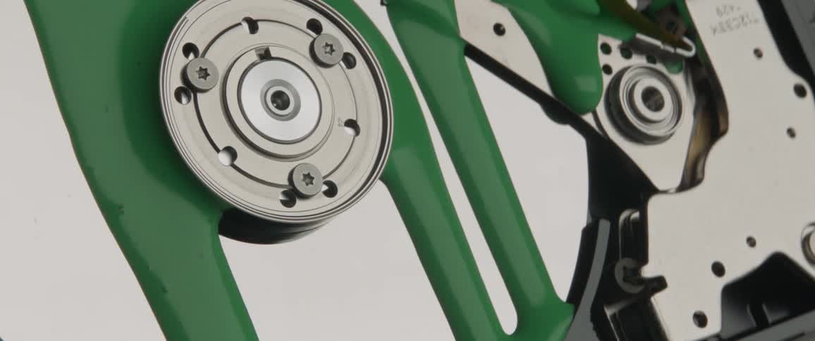 Thick green paint slowly drips down a metallic interior surface of an exposed computer hard drive