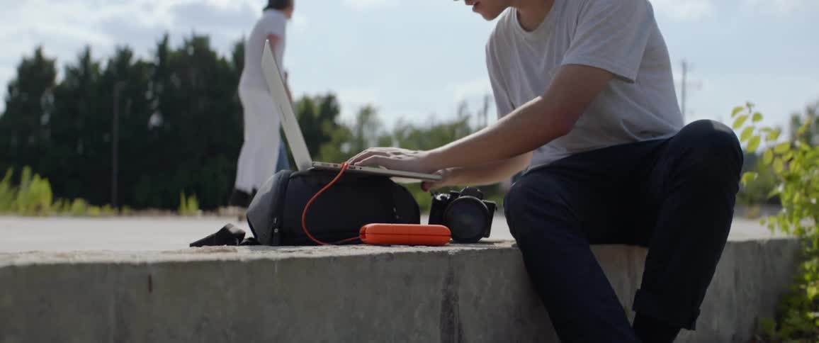A man sits on a ledge while uses a laptop