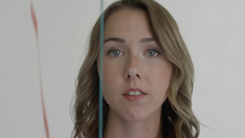 A young woman looks forward as different colored paint tickles steadily from above