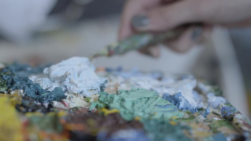 A woman is carefully spreading and mounding thick paint on a flat surface