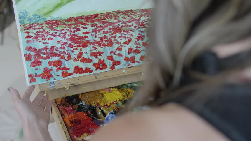 An artist using red paint to draw a field of flowers on a canvas