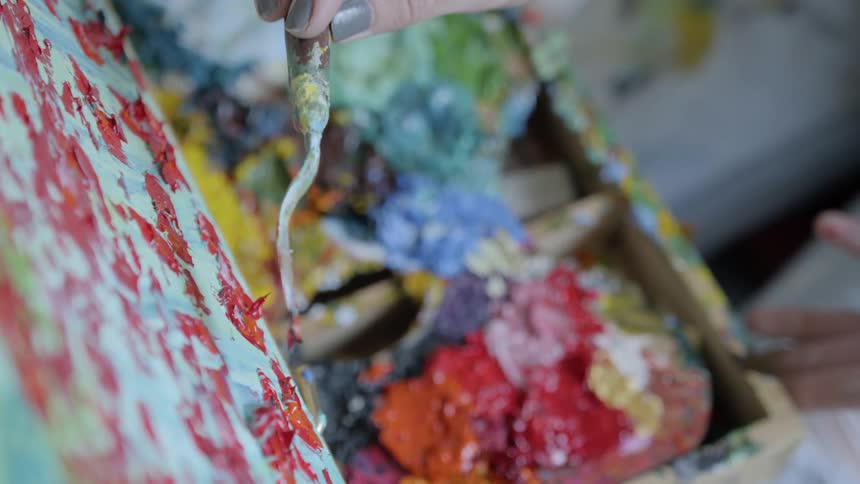 An artist dabs paint onto a canvas with a painting knife