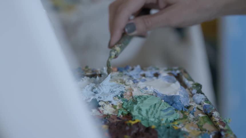 Woman mixes paint on palette with palette knife