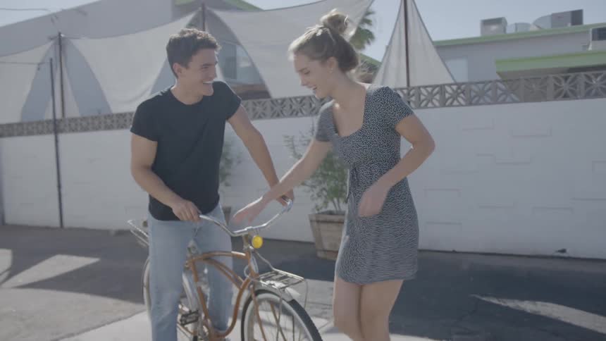 A man on a bicycle beckoning as a young woman approaches to sit on the front of the bike
