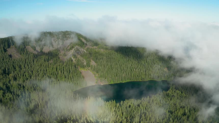 Clouds hang over forest covered slopes and a smooth lake