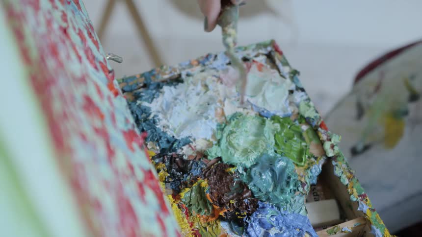A woman blends paint on a well used palette