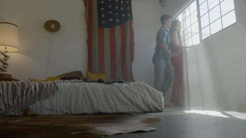 A man and woman stand beside each in a bedroom looking out a window