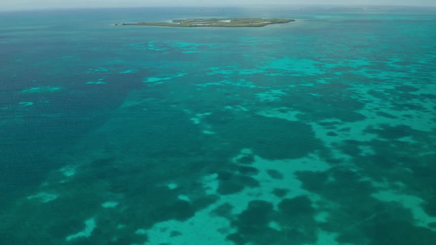 Clear blue tropical water with reefs leading to a small island