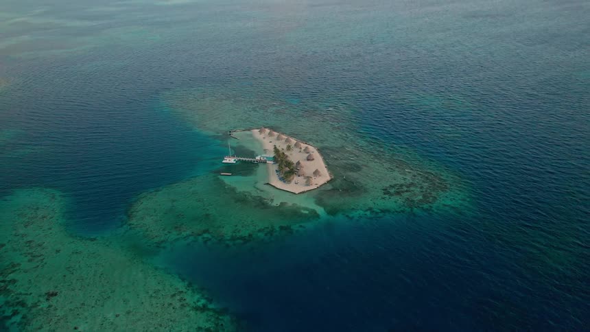 An island with a dock house and pool in the middle of clear blue water